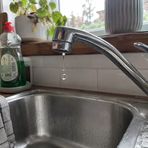 A kitchen tap dripping into a steel sink